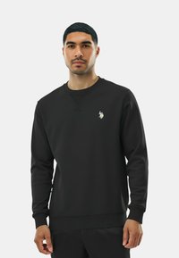 Felpa nera con scollo rotondo, maniche lunghe e piccolo logo ricamato sul petto. Tessuto liscio e design aderente.