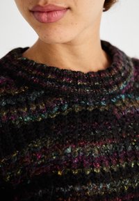 Knitted sweater featuring a textured, colorful pattern with black, purple, and green tones. Ribbed neckline adds detail.