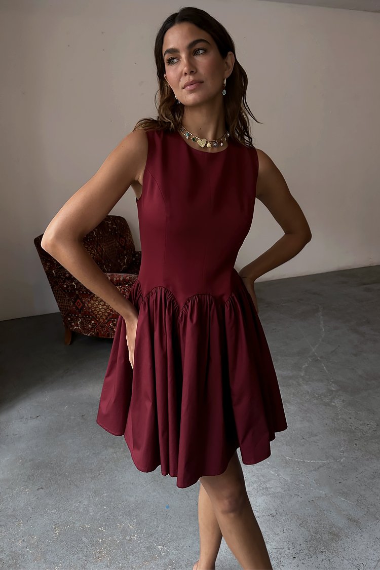 Robe sans manches bourgogne avec un corsage ajusté et une jupe évasée, présentant des détails froncés à la taille et une texture de tissu lisse.