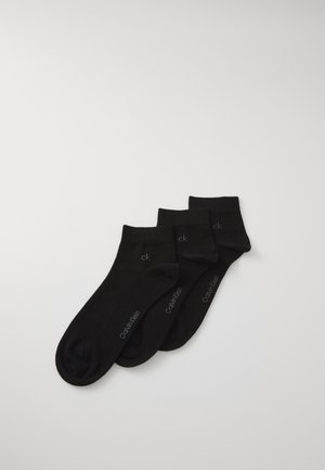 Three pairs of black ankle socks with "ck" and "Calvin Klein" logos stacked on a white background.