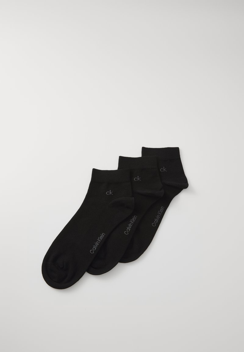 Három pár fekete bokaszakáll, rajtuk a "ck" és a "Calvin Klein" logókkal, egy fehér háttéren halmozva.