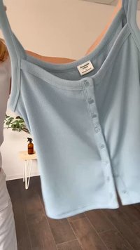 Top in cotone azzurro chiaro a costine, con scollatura tonda, quattro bottoni frontali e spalline. Il tessuto appare morbido e elasticizzato.