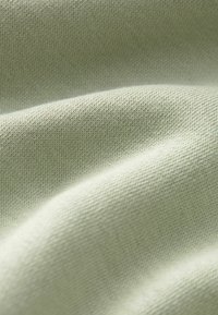 Tejido verde claro con un punto fino y texturizado, que muestra una superficie suave con suaves pliegues y un ligero brillo.