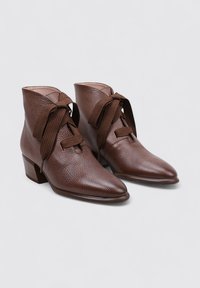 Botas de tobillo marrones hechas de cuero texturizado con punta afilada, que cuentan con un tacón bloque de altura media y cordones de tela.