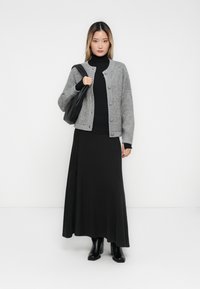Šedý pletený cardigan s žebrovaným lemem, zapínání na knoflíky, nošený přes černý rolák a splývavou černou maxi sukni, doplněný černými botami.