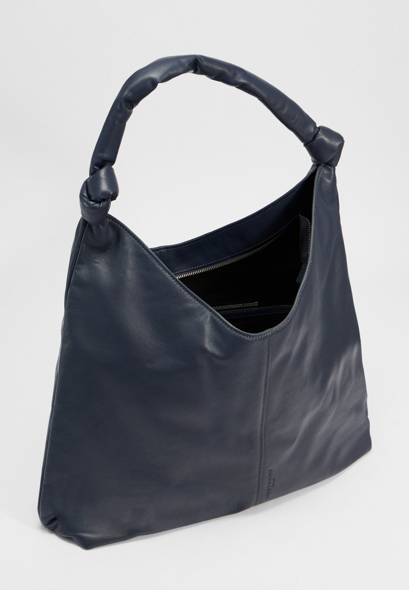 Ledertasche in dunklem Marineblau. Weiche Textur, einzigartiger Knotengriff und ein offenes Design mit einer Innenreißverschlusstasche zur Organisation.