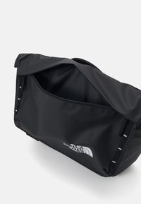 Marsupio nero North Face con il coperchio superiore aperto, che mostra il compartimento interno con zip su uno sfondo bianco uniforme.