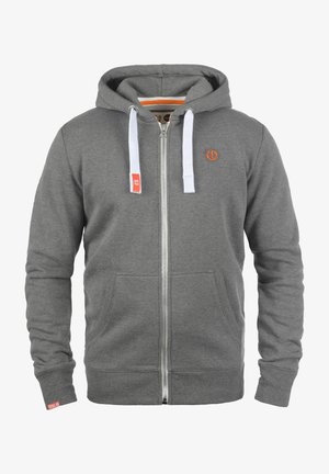 Haut à zip gris en matériau en coton, doté de cordons blancs, de poches avant et d'un détail de logo orange sur la poitrine.