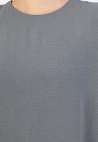 Tessuto grigio con una consistenza liscia, caratterizzato da un collo rotondo e maniche corte, che mostra un colore uniforme e costante senza motivi.