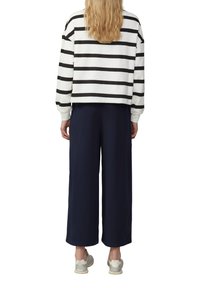 Wit en zwart gestreepte cropped sweatshirt, gecombineerd met marineblauwe wijde broek en lichtgrijze sneakers, gezien vanuit de achterkant.