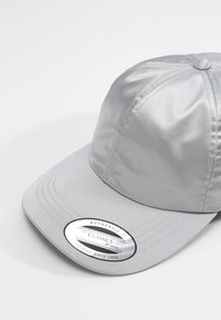 Sølv satin baseball cap med en buet skygge, der har et rundt mærke på fronten, der står "AUTHENTIC THE CLASSICS YUPONG SINCE 1974."