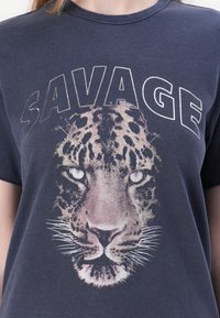 T-shirt nera con una grande e dettagliata grafica del volto di un leopardo, con la parola "SAVAGE" sopra, in lettere metalliche in grassetto.