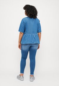 Top de mezclilla con mangas cortas y cintura peplum, combinado con jeans ajustados azules y zapatillas grises. El conjunto presenta un estilo casual.