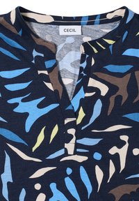 Granatowa bluzka z abstrakcyjnymi wzorami w odcieniach niebieskiego, brązowego i zielonego. Posiada dekolt z wycięciem i miękką teksturę. Etykieta marki: CECIL.