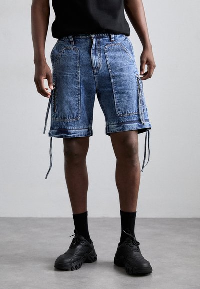 Shorts cargo din denim de culoare albastru deschis, cu buzunare frontale, curele laterale ajustabile și o croială lejeră. Asortați cu adidași negri și șosete.