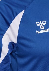 Maillot de sport bleu avec un panneau latéral blanc et un logo hummel blanc sur la poitrine montrant un dessin stylisé d'abeille.