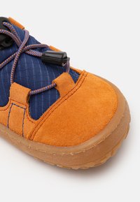Chaussure en textile bleu avec des accents en daim orange. Caractéristiques de laçage élastique noir et semelle en caoutchouc. La vue rapprochée met en avant la texture et les coutures.