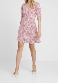 Rode bloemenjurk met een V-hals en korte mouwen, voorzien van een uitlopend rokje en kleine witte bloemen tegen een effen achtergrond.