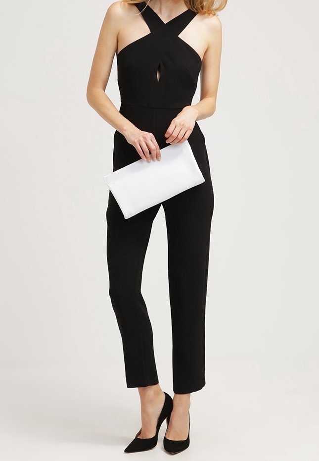 Black jumpsuit with a crisscross design and keyhole detail, paired with a white clutch and black pointed-toe heels. Smooth texture, fitted shape.