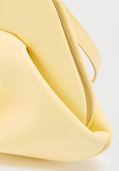 Coin d'un sac à main en cuir jaune doux avec des coutures visibles et une base arrondie sur un fond blanc.