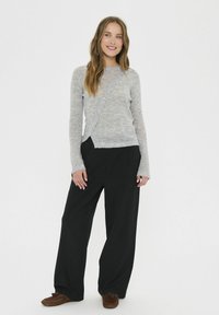 Cardigan lungo grigio chiaro con maniche lunghe e chiusura a bottoni, abbinato a pantaloni neri larghi e pantofole in suede marrone. Tessuto liscio, vestibilità casual.