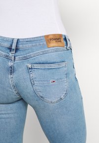 Světle modré džíny Tommy Jeans s kapsou na zadní straně a koženou nášivkou, nošené s bílým žebrovaným topem.