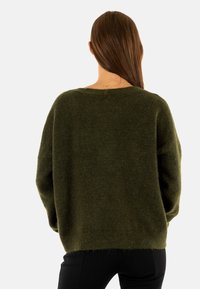 Maglione a maglia verde oliva con una vestibilità ampia, spalle basse e un ampio scollo. Morbido al tatto e con dettaglio a coste sull'orlo inferiore.