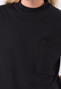 Svart bomullströja med rund halsringning och korta ärmar. Inkluderar en bröstficka med rektangulär form och mjuk textur.