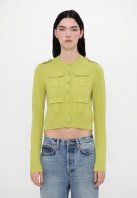 Cropped, buttoned cardigan in bright green knit with two front pockets, ribbed cuffs, and shoulder buttons. Paired with light blue denim.