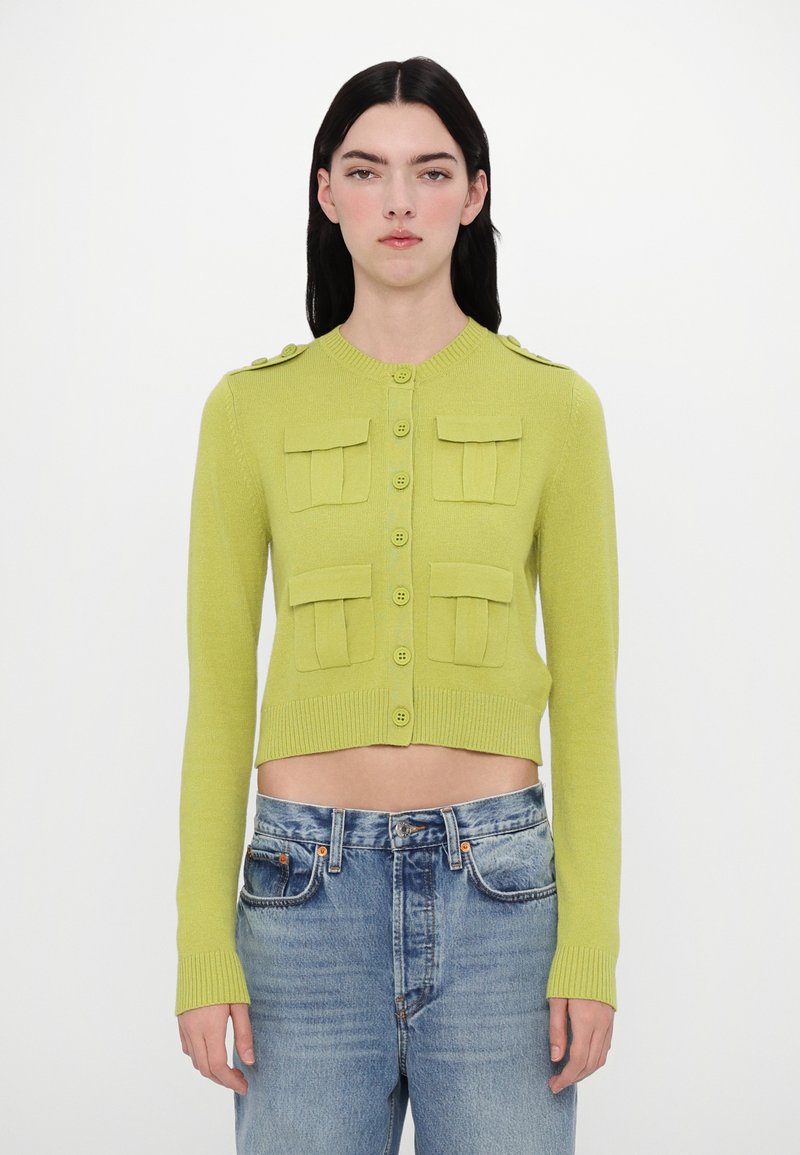 Cropped, buttoned cardigan in bright green knit with two front pockets, ribbed cuffs, and shoulder buttons. Paired with light blue denim.