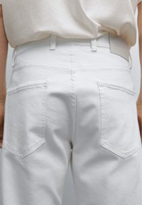 Jean en denim blanc avec un design légèrement structuré, comprenant deux poches arrière et une ceinture visible. La texture semble lisse et sans ornements.