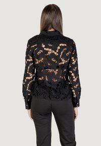 Zwarte kanten blouse met bloemen uitgesneden patronen, lange mouwen en een kraag. Heeft knoopmanchetten en doorzichtige secties.