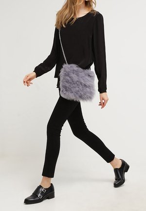 Grå fuskpäls crossbody-väska med silverkedjesnor, rektangulär form, mjuk textur, bärs av en person i svart klädsel.