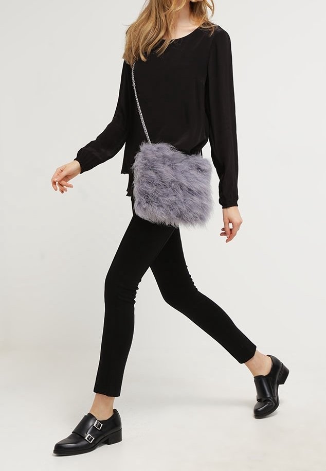 Szara torebka crossbody z sztucznego futra z silwerską łańcuszkową rączką, prostokątnego kształtu, o miękkiej teksturze, noszona przez osobę w czarnym ubraniu.