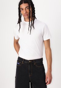 Hvid bomulds T-shirt med korte ærmer, parret med sorte cargo bukser med gult stikning og sidelommer. Enkel og klassisk design.