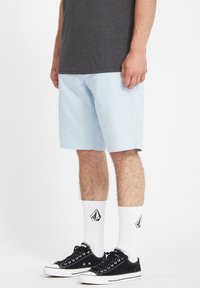 Light blue cotton shorts with a straight cut, paired with black sneakers and white crew socks featuring a logo, worn with a gray T-shirt.