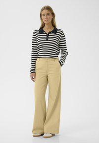 Polo à manches longues noir et blanc rayé, associé à un pantalon large beige. Comprend un col et une patte de boutonnage. Texture de tissu lisse.