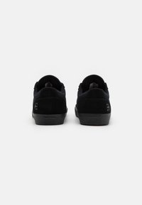 Black suede shoes with a low profile and rounded heel. Features minimal branding and textured rubber outsole. Clean and simple design.
