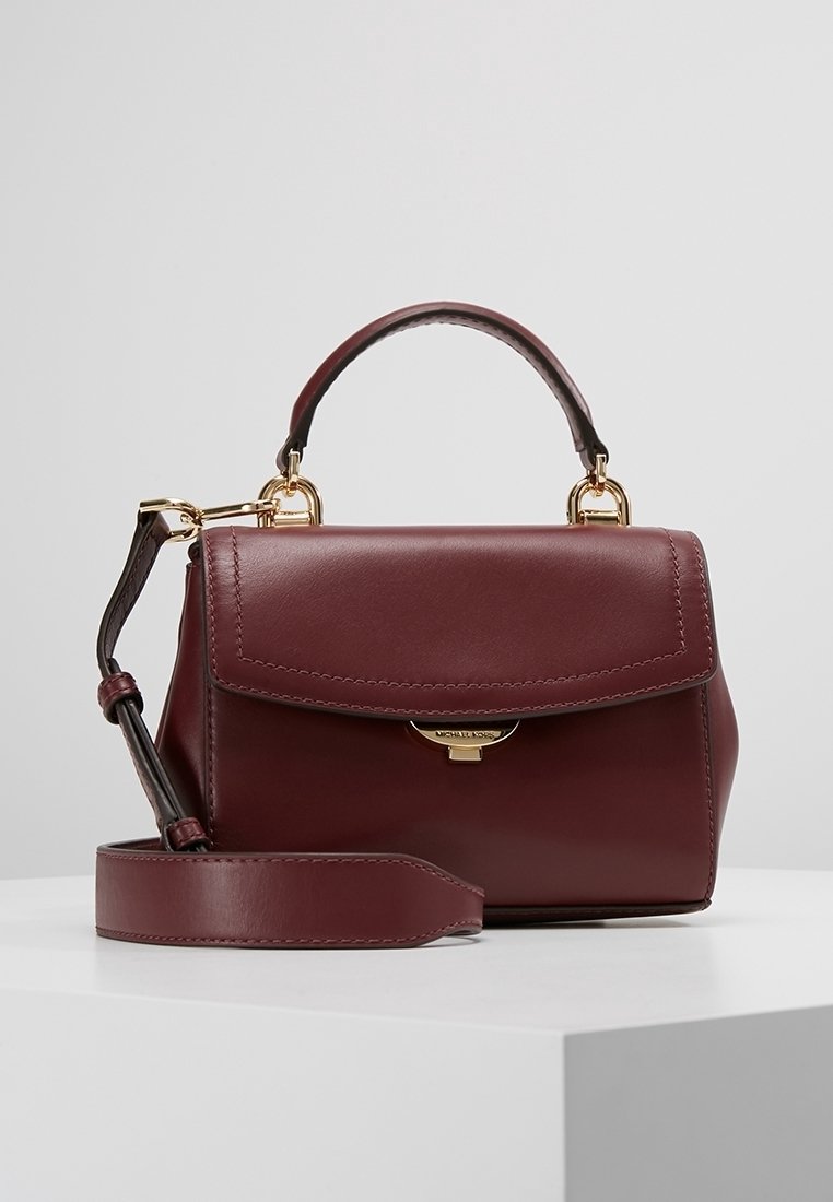 Burgundy læder håndtaske med en struktureret form, top håndtag, aftagelig skulderrem og hardware i guldfarve. Har en klaplukning.