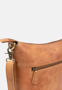 Hellbraune Ledertasche mit glatter Oberfläche, ausgestattet mit einem Reißverschluss und einem abnehmbaren Riemen mit Metallverschluss. Seitliche Reißverschlusstasche sichtbar.