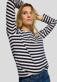 Navy and cream striped long-sleeve top with a smooth texture, round neckline, and relaxed fit, paired with blue jeans.