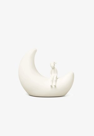 Hvit halvmåne-skulptur med en liten sittende figur som har på seg en sovelue på månens indre kurve mot en ensfarget hvit bakgrunn.