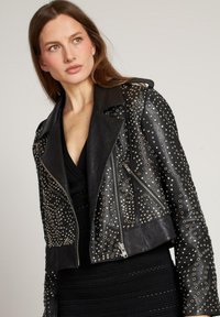 Giacca da moto cropped in pelle nera caratterizzata da borchie metalliche sulle spalle e sulle maniche, con tasche anteriori con zip e ampi rever.