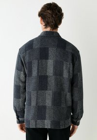 Šedá a černá kostkovaná košile s límečkem, dlouhými rukávy, knoflíkovými detaily a měkkou, texturovanou tkaninou.