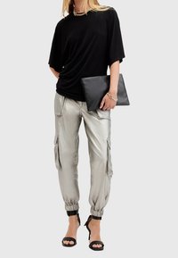 Czarna oversize'owa koszulka, metaliczne srebrne spodnie cargo z elastycznymi mankietami, czarna torebka kopertówka i czarne sandały na obcasie z paskami.