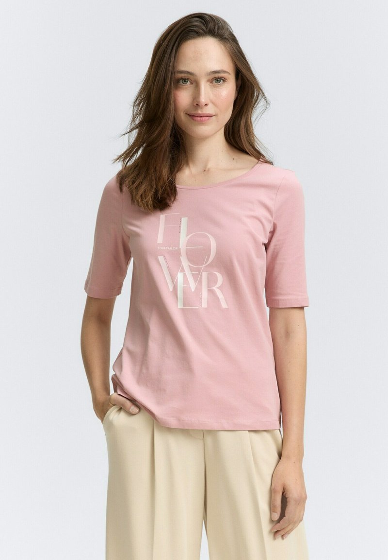 Helles rosa Baumwoll-T-Shirt mit kurzen Ärmeln und rundem Ausschnitt, versehen mit weißen Textgrafiken in moderner Schriftart. Glatte Textur.