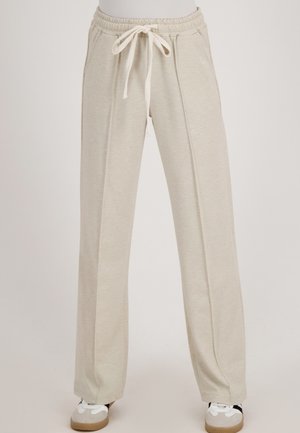 Beige wijde sweatpants met gestikte voornaden, elastische tailleband en koord, gedragen met witte en grijze casual schoenen.