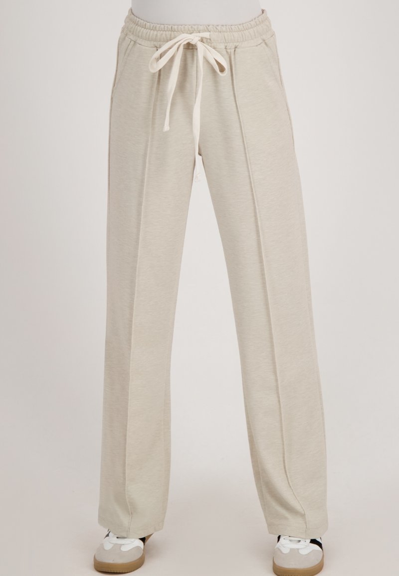 Beige wijde sweatpants met gestikte voornaden, elastische tailleband en koord, gedragen met witte en grijze casual schoenen.