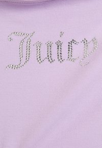 Fioletowa tkanina o gładkiej fakturze zdobi słowo „Juicy” wykonane z błyszczących, srebrnych kryształków, prezentując zabawny, dekoracyjny wzór.