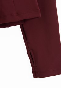 Κοντινό πλάνο ενός μακρυμάνικου μωβ-καφέ (burgundy) με τρύπα για τον αντίχειρα στη μανσέτα, που δείχνει την υφή του υφάσματος και τις λεπτομέρειες της ραφής.